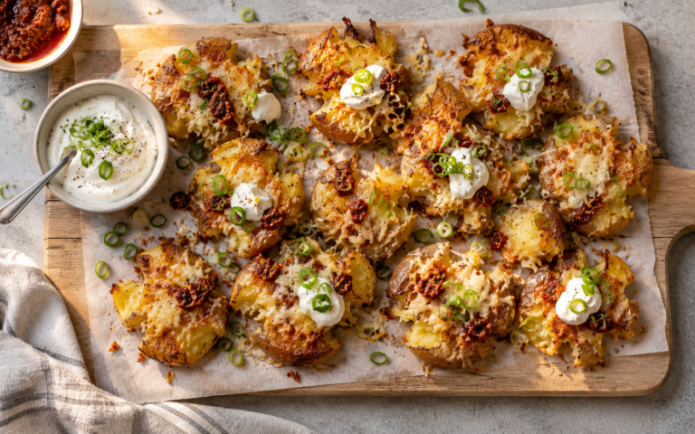 Crispy smashed potatoes med ost, rød pesto, rømme og vårløk servert som tilbehør